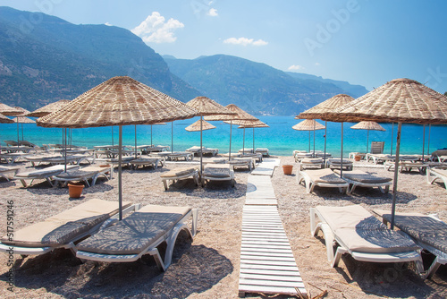 Landscape of beautiful coastline in Oludeniz with straw umbrellas. View from beach on blue sea and mountains  amazing rest in Turkey. Beginning of day on beach without people.