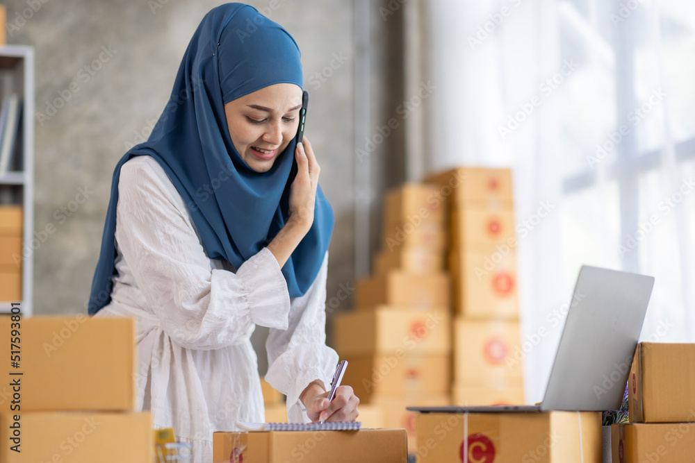 Muslim young Asian woman working at home doing sme ecommerce online small business entrepreneur checking postal parcels to delivery to online customers, startup Muslim Sme business concept. Muslim young Asian woman working at home doing sme ecommerce online small business entrepreneur checking postal parcels to delivery to online customers, startup Muslim Sme business concept.