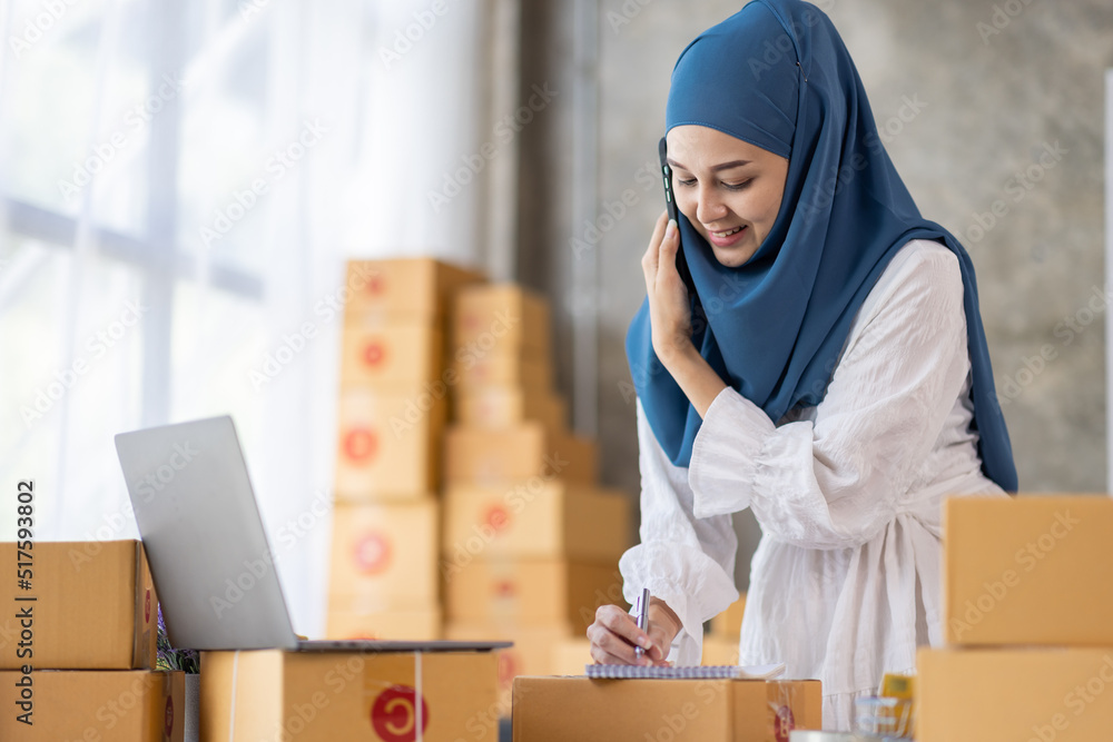 Muslim young Asian woman working at home doing sme ecommerce online small business entrepreneur checking postal parcels to delivery to online customers, startup Muslim Sme business concept. Muslim young Asian woman working at home doing sme ecommerce online small business entrepreneur checking postal parcels to delivery to online customers, startup Muslim Sme business concept.