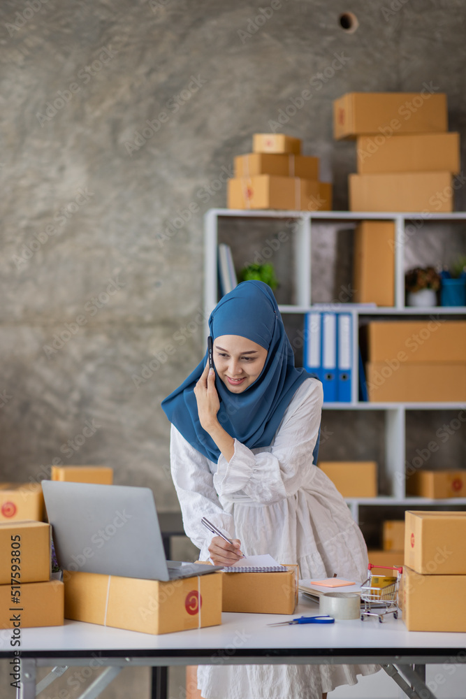 Muslim young Asian woman working at home doing sme ecommerce online small business entrepreneur checking postal parcels to delivery to online customers, startup Muslim Sme business concept. Muslim young Asian woman working at home doing sme ecommerce online small business entrepreneur checking postal parcels to delivery to online customers, startup Muslim Sme business concept.