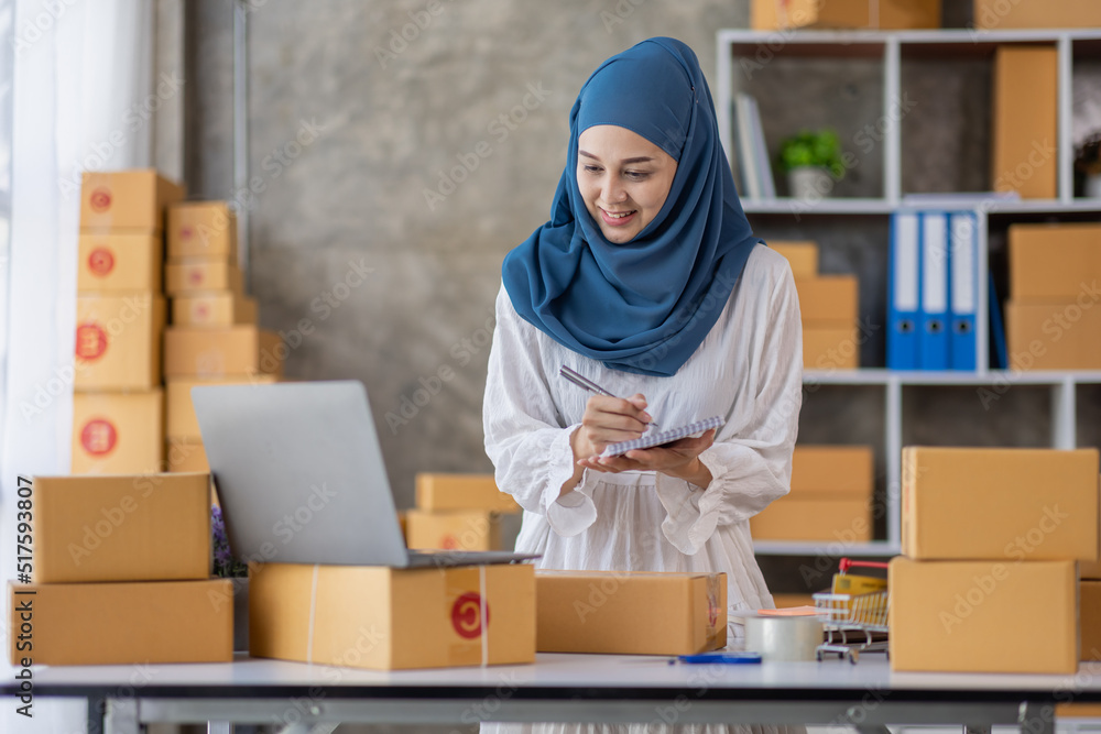 Muslim young Asian woman working at home doing sme ecommerce online small business entrepreneur checking postal parcels to delivery to online customers, startup Muslim Sme business concept. Muslim young Asian woman working at home doing sme ecommerce online small business entrepreneur checking postal parcels to delivery to online customers, startup Muslim Sme business concept.