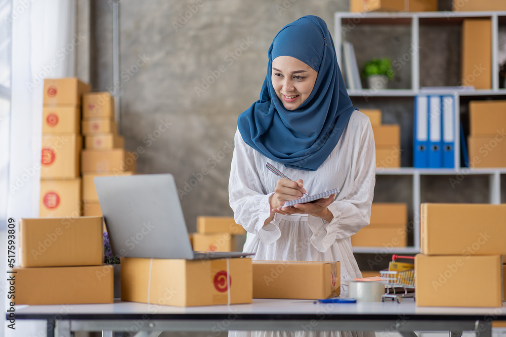 Muslim young Asian woman working at home doing sme ecommerce online small business entrepreneur checking postal parcels to delivery to online customers, startup Muslim Sme business concept. Muslim young Asian woman working at home doing sme ecommerce online small business entrepreneur checking postal parcels to delivery to online customers, startup Muslim Sme business concept.