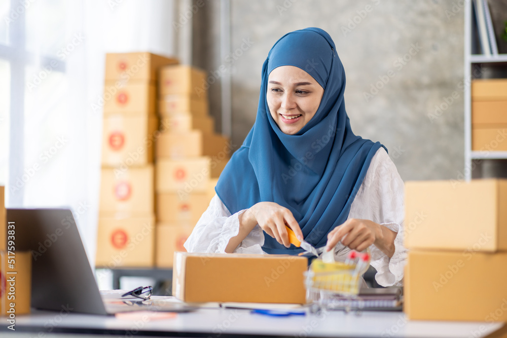 Muslim young Asian woman working at home doing sme ecommerce online small business entrepreneur checking postal parcels to delivery to online customers, startup Muslim Sme business concept. Muslim young Asian woman working at home doing sme ecommerce online small business entrepreneur checking postal parcels to delivery to online customers, startup Muslim Sme business concept.