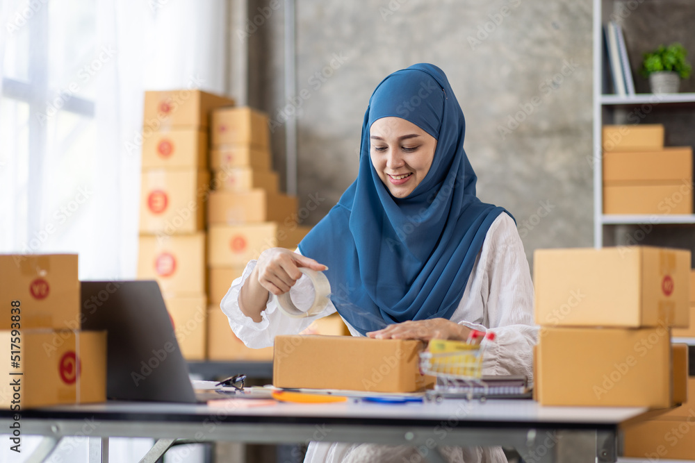 Muslim young Asian woman working at home doing sme ecommerce online small business entrepreneur checking postal parcels to delivery to online customers, startup Muslim Sme business concept. Muslim young Asian woman working at home doing sme ecommerce online small business entrepreneur checking postal parcels to delivery to online customers, startup Muslim Sme business concept.