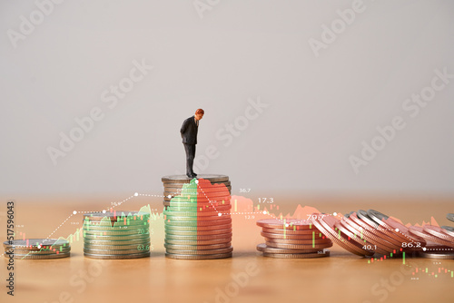 Miniature figure standing on highest coins stacking with increasing and decreasing stock market graph and chart for Business investment growth and Economic recession concept. photo
