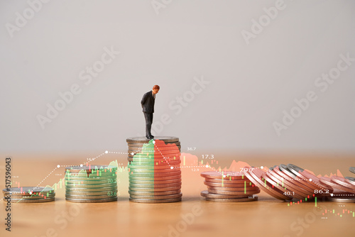 Schilderij op canvas Miniature figure standing on highest coins stacking with increasing and decreasing stock market graph and chart for Business investment growth and Economic recession concept
