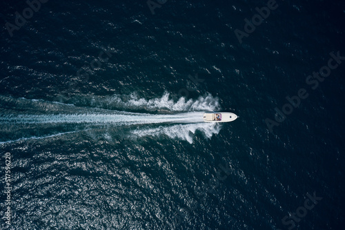 White speedboat on black water top view. White boat moving fast in the ocean aerial view.