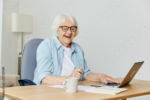 a happy elderly woman laughs happily during a video call on a laptop while sitting at her desk at home
