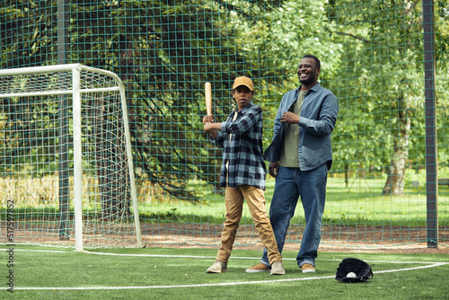 Canvas Print African happy dad learning his son to play baseball on the field outdoors