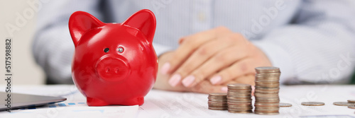 Person accountant on working place, stack of coins, red piggy bank photo