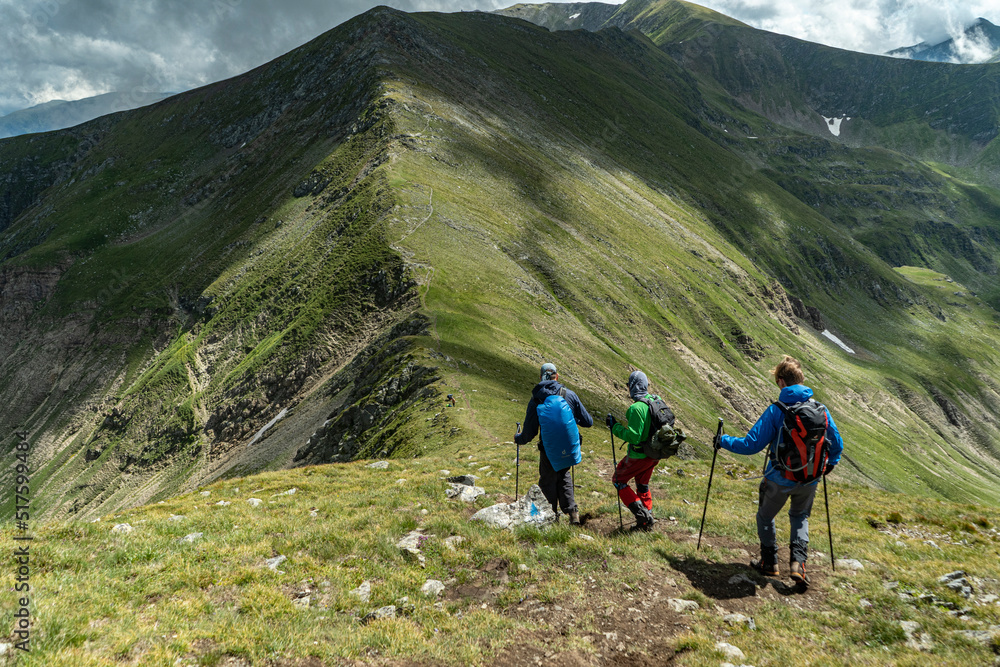 three tourists descending from a mountain with mountain ridge on backgorund