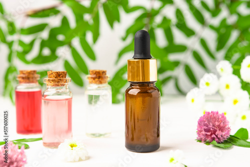 Bottles with flower extracts on a white table with flowers and leaves of the plant. Essential oil for massage and aromatherapy with natural ingredients.