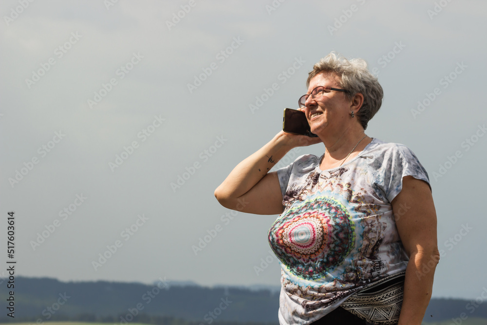 Portrait of smiling caucasian senior woman in glasses talking on cellphone on the vacation in mountains.