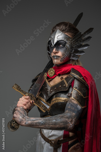 Portrait of ancient warrior woman dressed in red cape and dark armor holding sword.