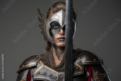 Tablou canvas Antique female knight dressed in steel armor holding sword near her face