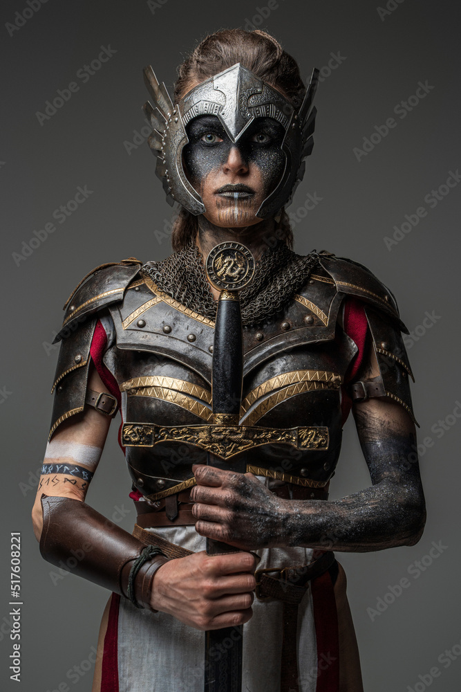 Antique female knight dressed in steel armor holding sword against dark background. - obrazy, fototapety, plakaty 
