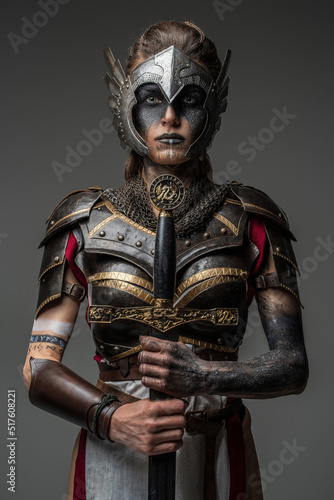 Antique female knight dressed in steel armor holding sword against dark background.