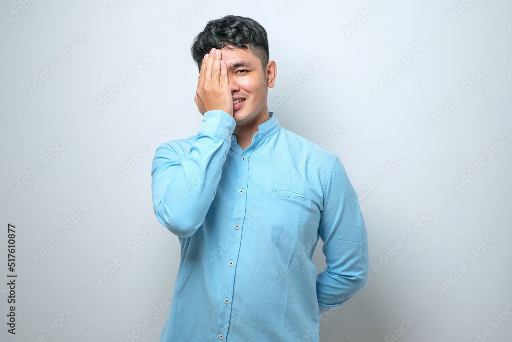 Young handsome asian man covering one eye with hand, confident smile on face and surprise emotion. Young handsome asian man covering one eye with hand, confident smile on face and surprise emotion.