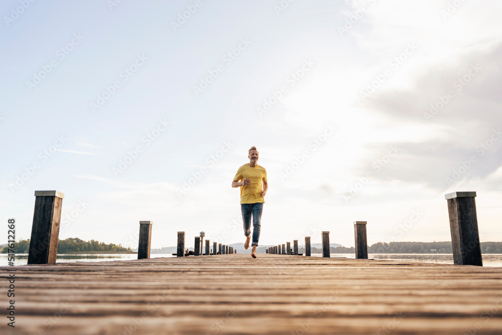 Carefree mature man running on pier in front of sky Carefree mature man running on pier in front of sky