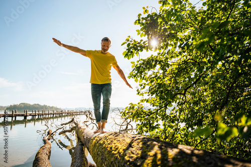 Mature man balancing on fallen tree at lakeshore