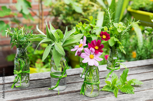 Fresh herbs and flowers in decorated glass bottles standing on balcony table photo