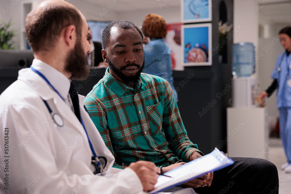 Fototapeta premium Medic physician talking to male patient in waiting room, using medical checkup report to give disease diagnosis and treatment. Doctor and man doing healthcare consultation at clinic.