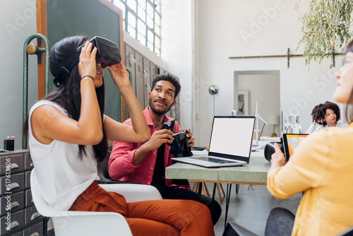 Businesswoman watching VR goggles by colleague at workplace photo