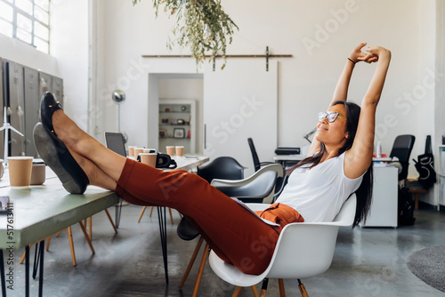 Smiling businesswoman stretching arms on chair at workplace photo