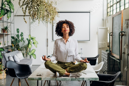 Young businesswoman meditating on desk at office photo