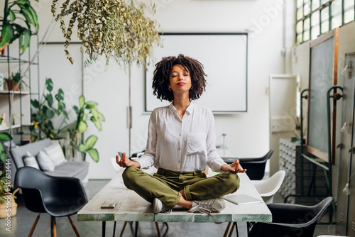 Young businesswoman meditating on desk at office