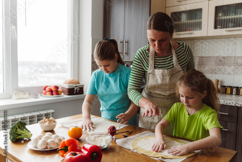Mother assisting daughters to prepare pizza in kitchen at home