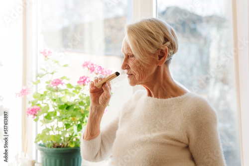 Senior woman smelling palo santo stick at home photo