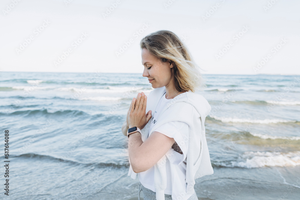 Happy woman with hands clasped standing in front of sea
