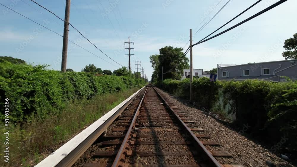 A low angle view moving straight down train tracks with green trees on either side. It runs through a suburban neighborhood on a sunny day. The drone camera dolly in directly over the empty tracks. A low angle view moving straight down train tracks with green trees on either side. It runs through a suburban neighborhood on a sunny day. The drone camera dolly in directly over the empty tracks.
