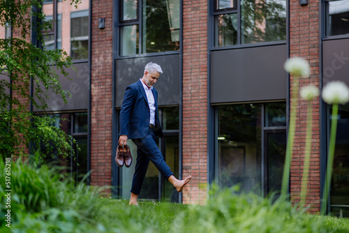 Businessman walking barefoot in park, feeling free, work life balance concept. photo