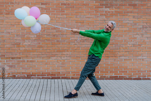 Fun portrait of happy energetic mature businessman holding balloons in street, feeling free, work life balance concept. photo