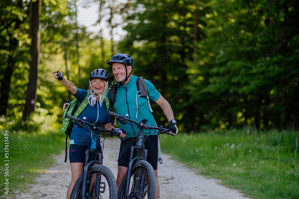 Obraz premium Portrait of active senior couple riding bicycles at summer park, standing on path and looking at camera