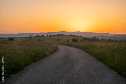 Road running through a mountain meadow towards the rising sun