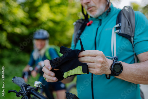 Close-up of senior man biker putting on bicycle gloves in nature.
