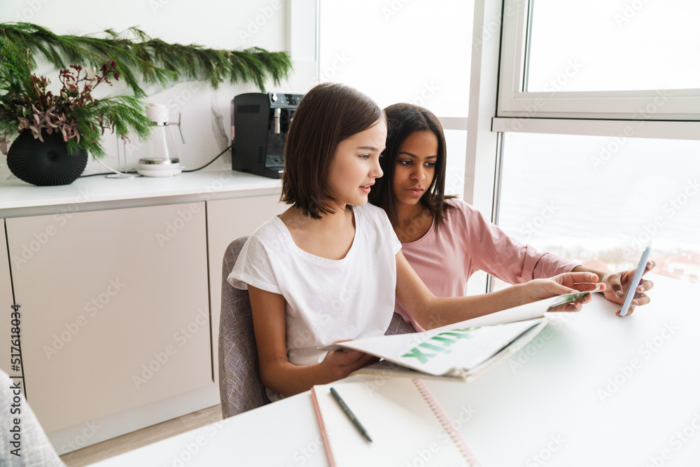 Multiracial sisters using cellphone while doing homework together