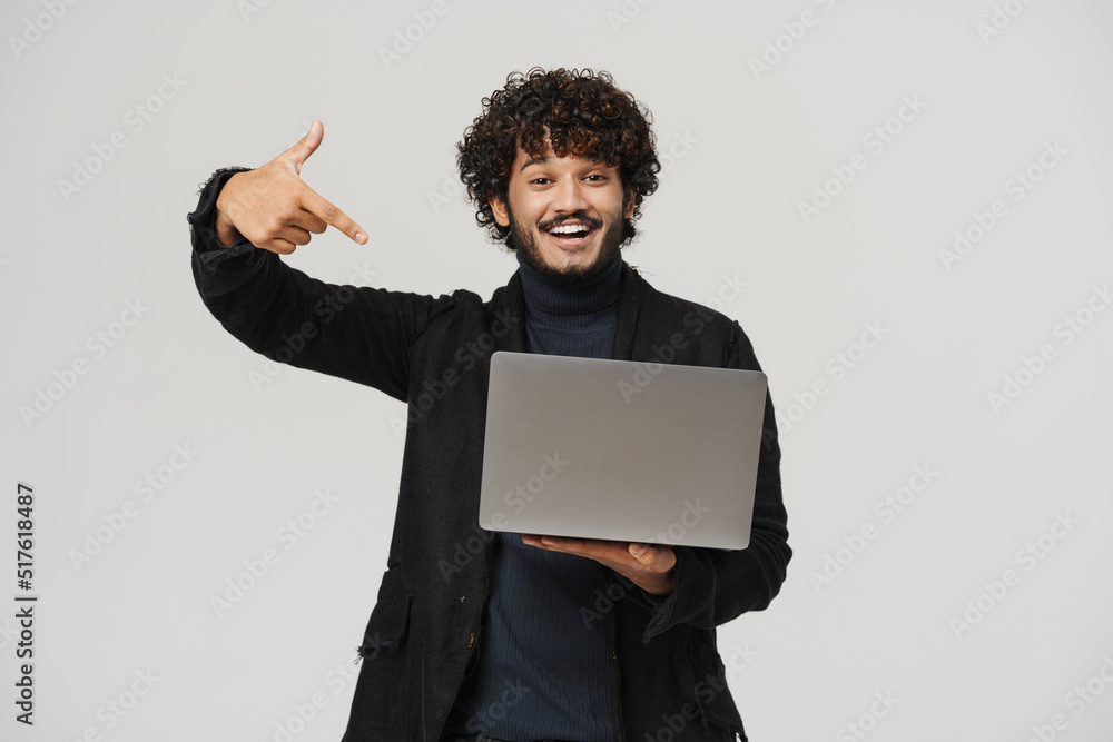 Adult indian smiling curly man pointing on laptop Adult indian smiling curly man pointing on laptop