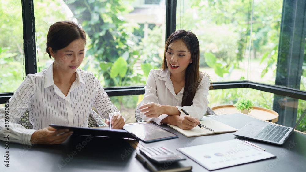 Coworker business concept, Two businesswoman discussing financial report and take notes on notebook Coworker business concept, Two businesswoman discussing financial report and take notes on notebook