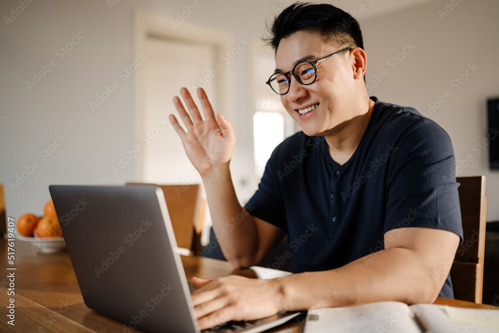 Adult smiling asian man with laptop waving at camera Adult smiling asian man with laptop waving at camera