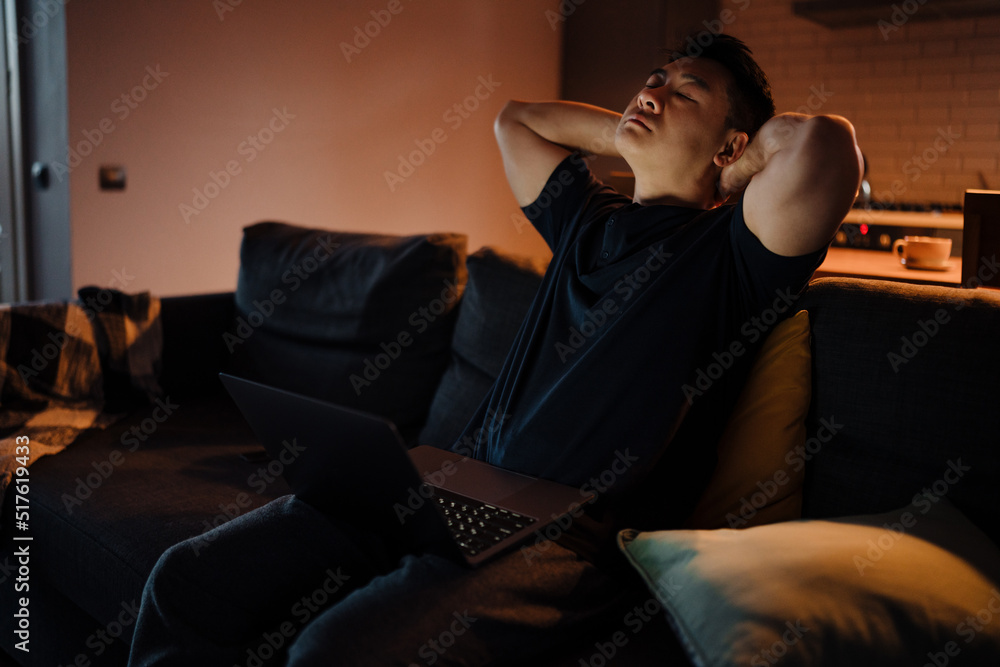 Fototapeta premium Adult asian man sitting on sofa with laptop