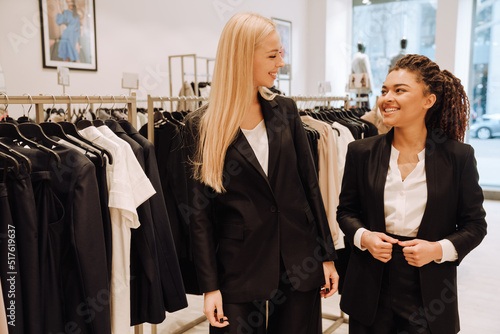 Happy saleswomen in uniform smiling while working in clothes store photo