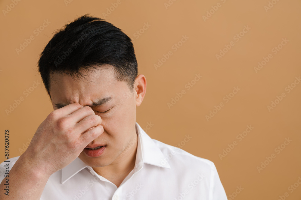 Brunette adult asian man wearing shirt touching his nose bridge Brunette adult asian man wearing shirt touching his nose bridge