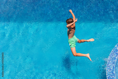 10 year old boy jumping into water in pool, having fun in summer vacation at hotel in health resort. Water sports and games, summer holiday concept.