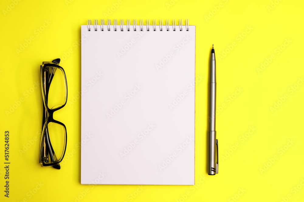 Top view on sketchbook and pen with eyeglasses on yellow background Top view on sketchbook and pen with eyeglasses on yellow background