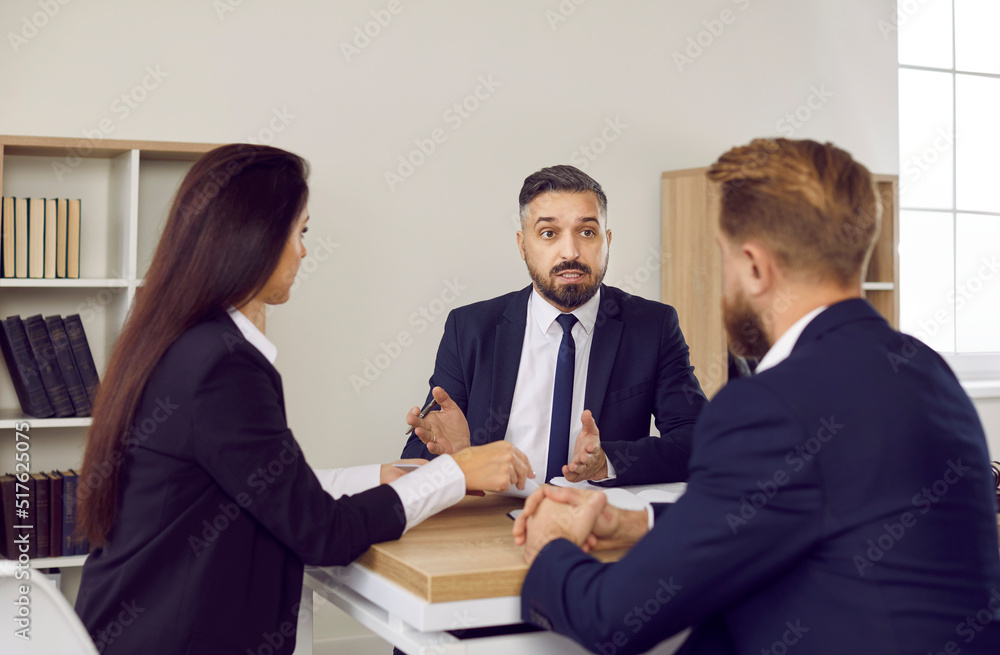 Legal advice. Business meeting in office of law firm of male lawyer and married couple of clients. Serious man in suit provides advice and talks to man and woman sitting in front of him at table. Legal advice. Business meeting in office of law firm of male lawyer and married couple of clients. Serious man in suit provides advice and talks to man and woman sitting in front of him at table.