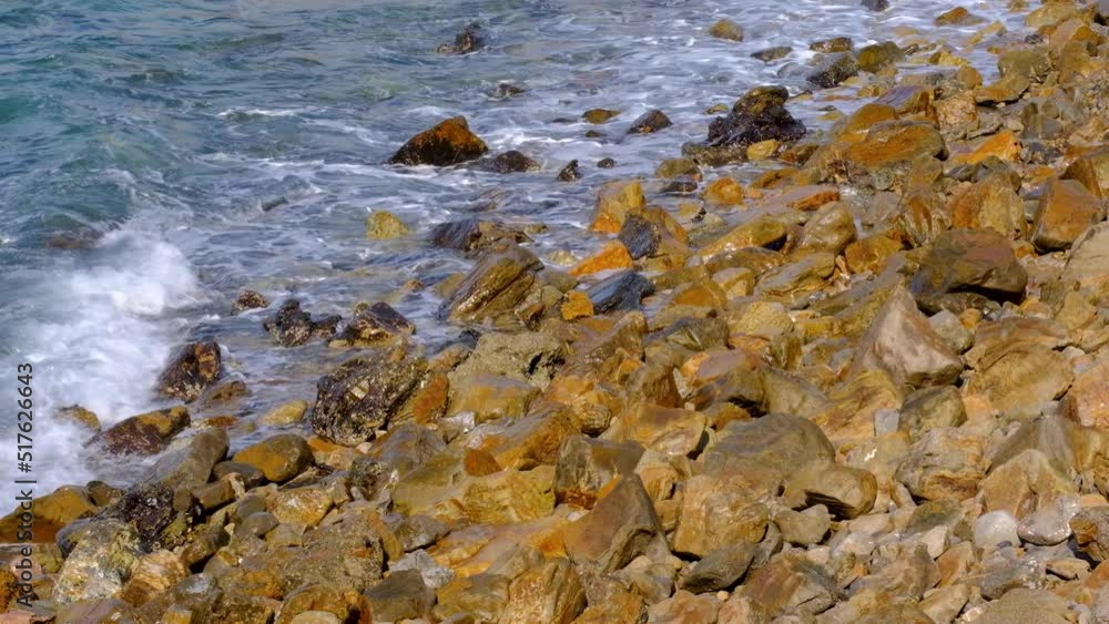 Ocean waves rolling in and crashing onto a remote, rugged and golden rocky coastal shoreline in the wilderness on a tropical island Ocean waves rolling in and crashing onto a remote, rugged and golden rocky coastal shoreline in the wilderness on a tropical island